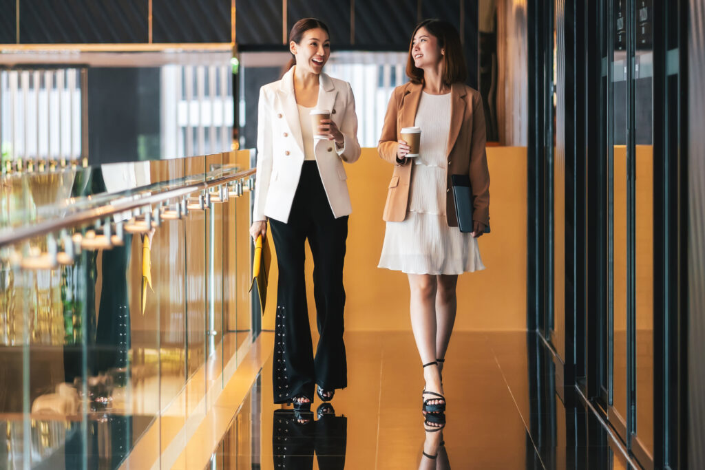 Two business women walking in a coworking space holding coffees.