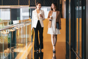 Two business women walking in a coworking space holding coffees.